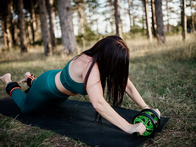 Woman using an ab wheel on a mat in a pine forest (illustrative photo)
