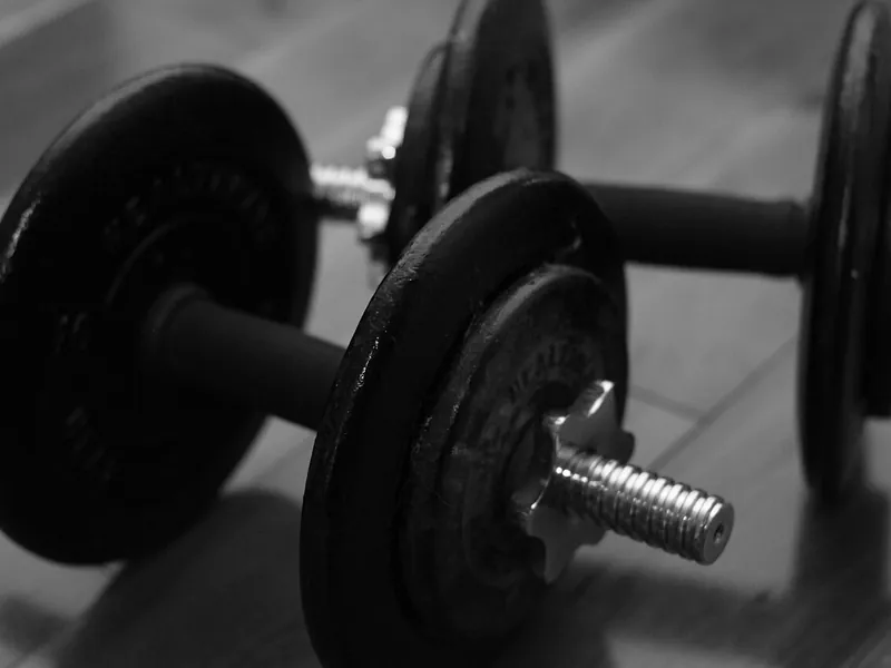 Adjustable plate dumbbells on a floor, black and white (illustrative photo)