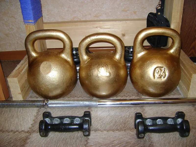 Three kettlebells and two dumbbells on a home gym floor (illustrative photo)