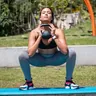 Woman holding a kettlebell in a squat on a mat outdoors (illustrative photo)