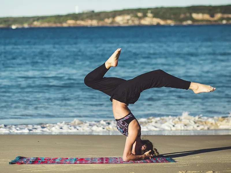Person in a headstand pose on a yoga mat on the beach (illustrative photo)