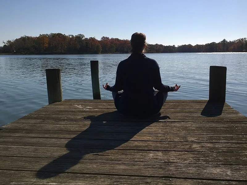 Person meditating at the end of a lakeside dock (illustrative photo)