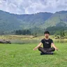 Man meditating cross-legged on grass by a mountain lake (illustrative photo)