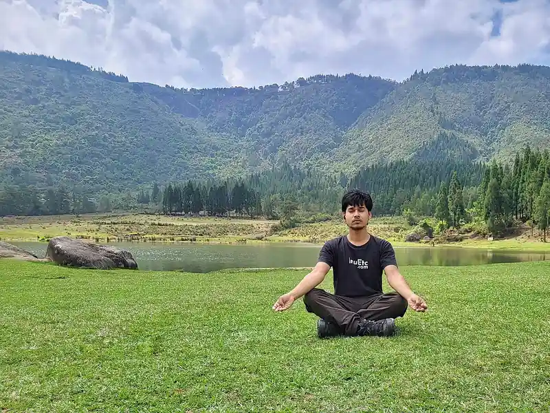 Man meditating cross-legged on grass by a mountain lake (illustrative photo)