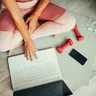 Woman on an exercise mat with a laptop, phone and small dumbbells (illustrative photo)
