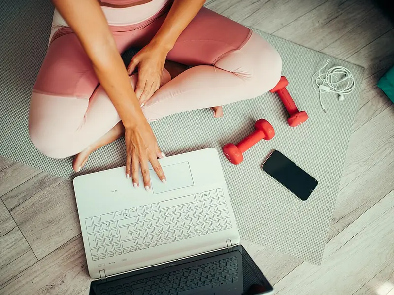 Woman on an exercise mat with a laptop, phone and small dumbbells (illustrative photo)